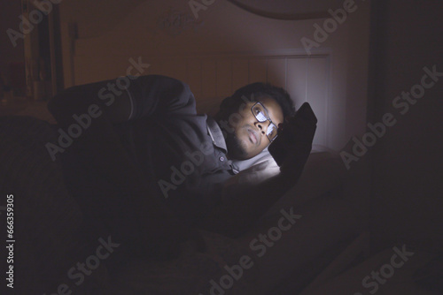 young man sitting on bed using smart phone at night 