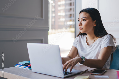 Pondering Asian woman working with laptop