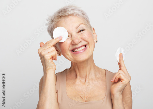 Photo of nice old woman use sponge remove make up over light grey background