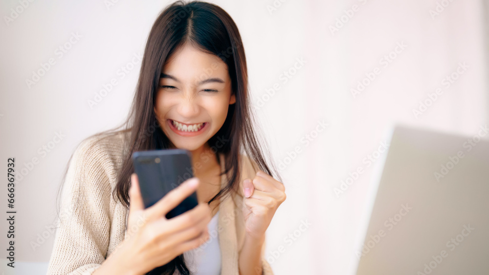 Young asian woman happy working on computer laptop and hand typing chat message on mobile smartphone at home. Video call, Online meeting Young asian woman happy working on computer laptop and hand typing chat message on mobile smartphone at home. Video call, Online meeting