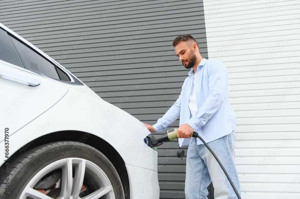 Stylish man inserts plug into the electric car charging socket Stylish man inserts plug into the electric car charging socket