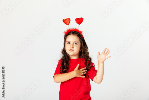 Smiling happy little girl in red t-shirt and headband with two red hearts celebrating Valentine's day on white. children's holiday card, gift for Mother's day, Father's day, hobby, crafts concept.