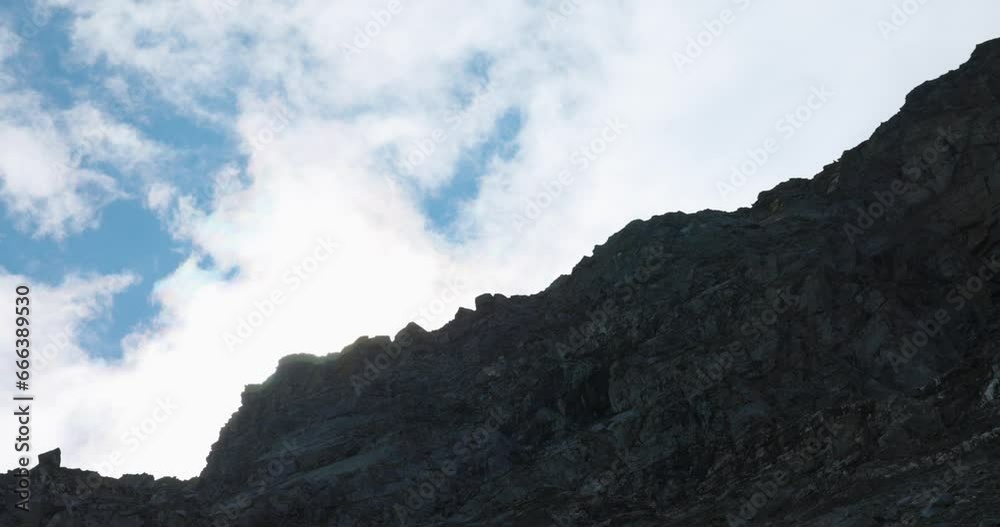 Cloudy blue sky over a rock ridge of a cliff. Looking up shot. Cloudy blue sky over a rock ridge of a cliff. Looking up shot.
