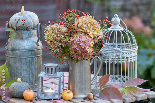 Herbst-Arrangement mit Blumenstrauß mit Hortensienblüten und Hagebutten, Kürbissen und Laterne