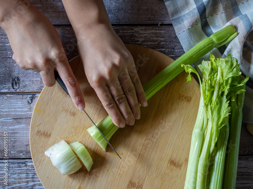 Concept of food handling, grabbing or taking food with hands. female hands preparing celery  over a wooden table, top view