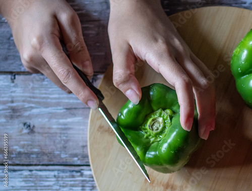 Concept of food handling, grabbing or taking food with hands. female hands preparing or cutting a green pepper over a wooden table, top view