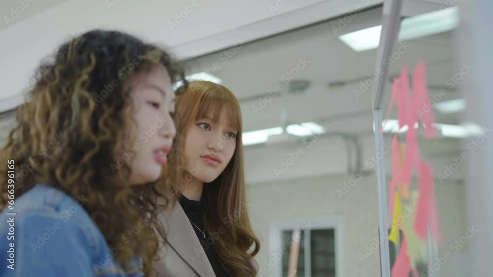 Asian creative business women are writing note on the text sheet after thinking new idea and planning project with colleague ,Two employee brainstorming idea on glass wall and sticky Asian creative business women are writing note on the text sheet after thinking new idea and planning project with colleague ,Two employee brainstorming idea on glass wall and sticky