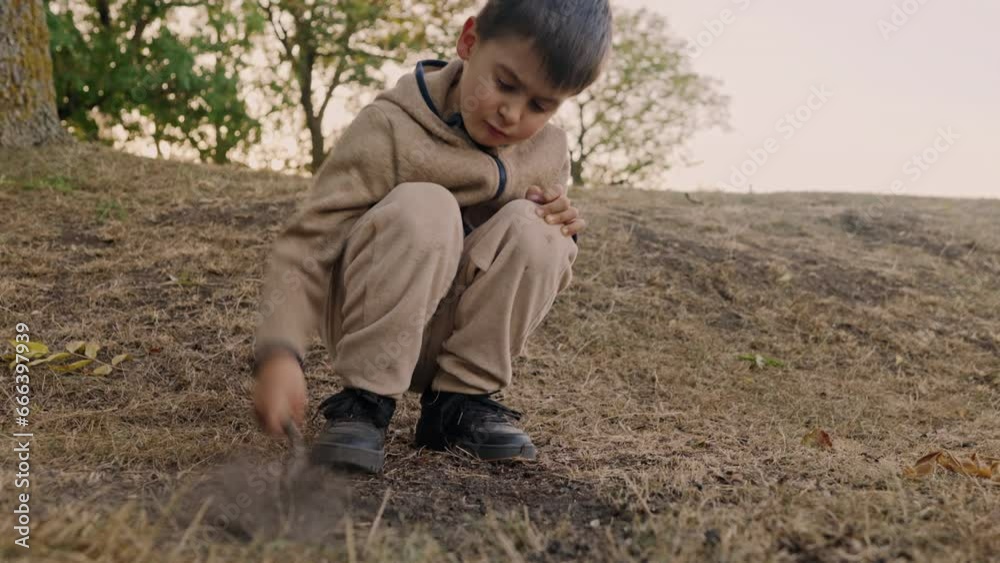 Caucasian little boy holding a stick and hitting the ground with it, playing during an outdoor walk with his family in the park. Adorable baby having fun Caucasian little boy holding a stick and hitting the ground with it, playing during an outdoor walk with his family in the park. Adorable baby having fun