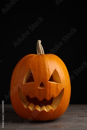 Scary jack o'lantern made of pumpkin on wooden table against black background. Halloween traditional decor