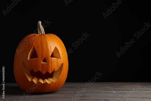 Scary jack o'lantern made of pumpkin on wooden table against black background, space for text. Halloween traditional decor