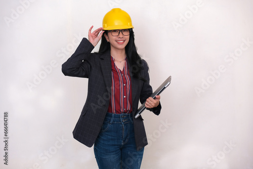 Female architect standing and holding a laptop, wearing yellow safety hard hat, ready to work photo