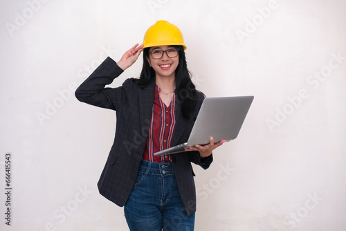 Female project engineer standing and holding yellow safety hard hat and a laptop in her left hand photo