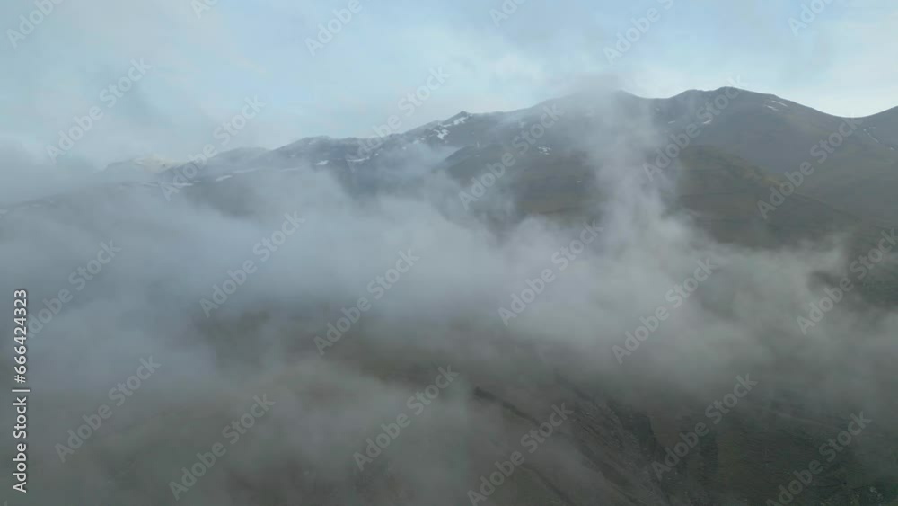 Gray rocky snowy mountains tops with no vegetation. Clouds flying slowly on the ground and between rocks against blue sky. Armenia, Lori. Drone video. Camera turn. Gray rocky snowy mountains tops with no vegetation. Clouds flying slowly on the ground and between rocks against blue sky. Armenia, Lori. Drone video. Camera turn.