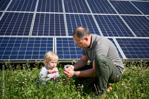 Young father showing to his little son how to use tools in background of solar panels. Dad teaching his child how to use screwdriver. Cute son and father learning tools on background of solar panels.
