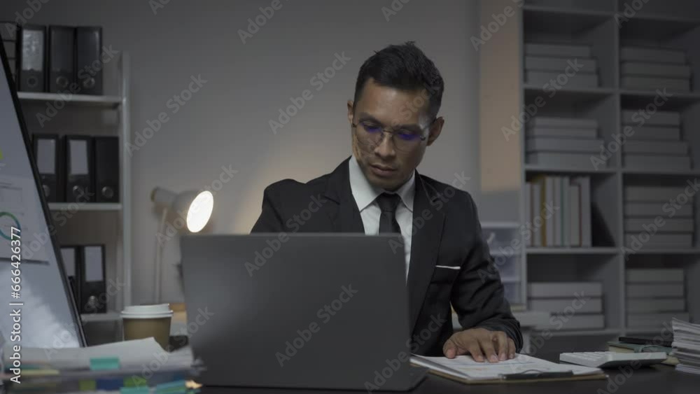 Serious Asian businessman working with paper and calculator for documents, financial graphing, calculating business accounting, savings, finance and analyzing world economy. Serious Asian businessman working with paper and calculator for documents, financial graphing, calculating business accounting, savings, finance and analyzing world economy.