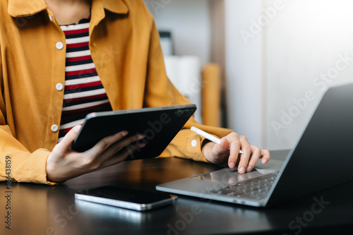 Hands of woman using mobile phone in modern office with laptop and digital tablet at home office photo