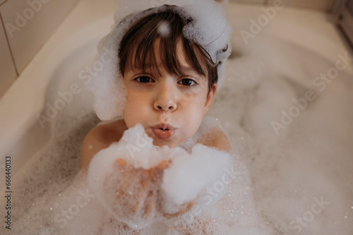 Cute boy blowing soap sud in bathroom at home photo