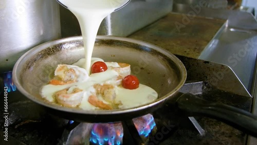 Chef drizzles heavy cream into pan on gas stove with shrimp , omatoes and milky white suace photo