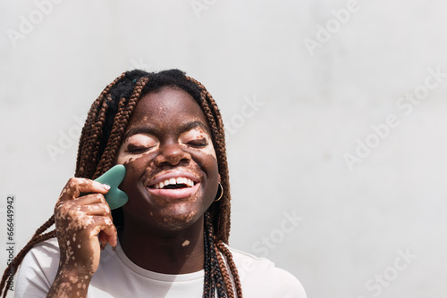 Happy young woman using gua sha in front of white wall photo