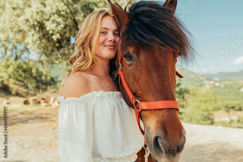 Young beautiful smiling girl with horse in countryside. Cowgirl enjoying with her horse outdoors.