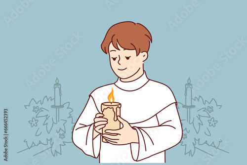 Boy participates in holy communion and holds burning candle for christian religious ritual in church. Child in clothes for communion ceremony in church smiles, wanting to become true believer catholic