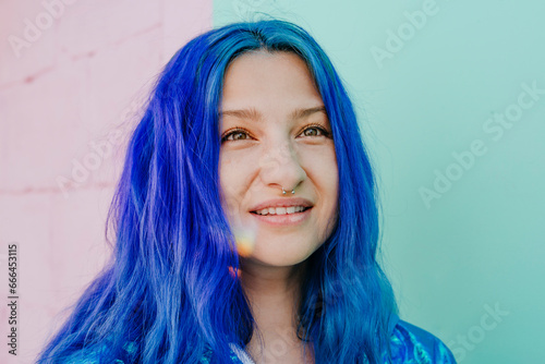 Smiling woman with blue dyed hair in front of wall photo