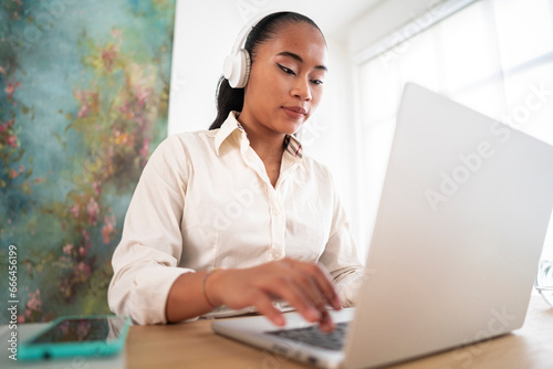Low angle of concentrated female employee listening to music on headphones while working in office using computer and typing information photo