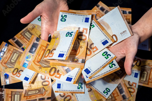 Financial success with hands presenting 50 Euro banknotes above a generous pile, symbolizing wealth, prosperity or financial management, against black backdrop, representation of abundance or opulence photo