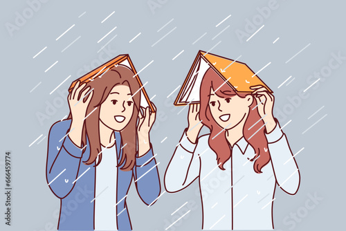 Women take shelter from rain under books and smile, rejoicing at onset of autumn season. Happy girls cover heads with textbooks to avoid getting wet during heavy rain or spring storm