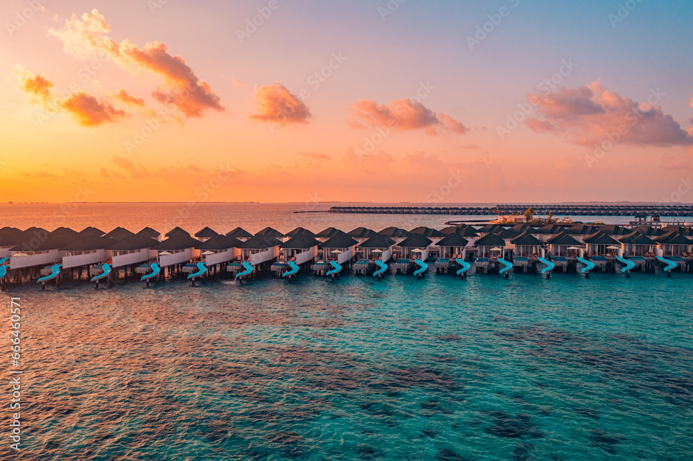 Obraz premium Aerial sunset panoramic landscape luxury tropical resort water villas. Beautiful island beach orange sunrise sea sky. Amazing bird eyes panorama Maldives paradise tropical bay. Exotic summer vacation 