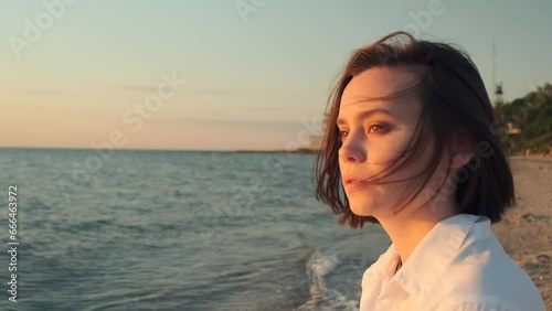 Portrait of beautiful young woman near the sea. Pretty girl looking at seascape with sun light on her face, female enjoying sunrise on beach. Side view