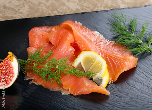 Smoked salmon on a black serving platter garnished with a thin slice of lemon, dill and a quarter of a fig
