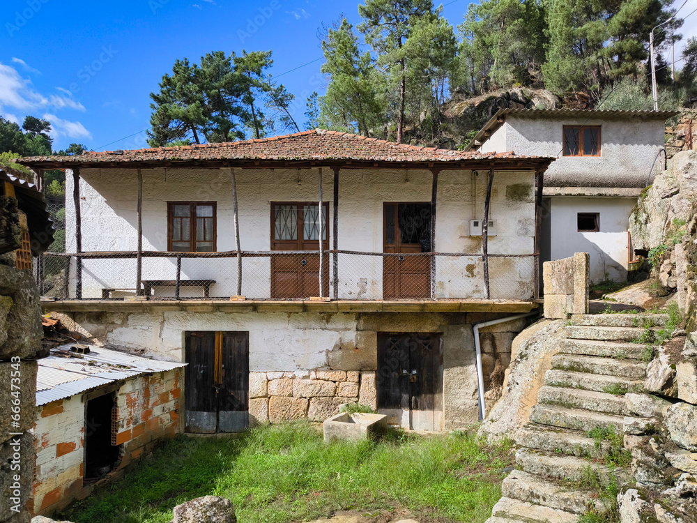 Pequeno bairro abandonado com algumas casas velhas e umas escadas em pedra de granito com um pinheiral ao fundo em Portugal