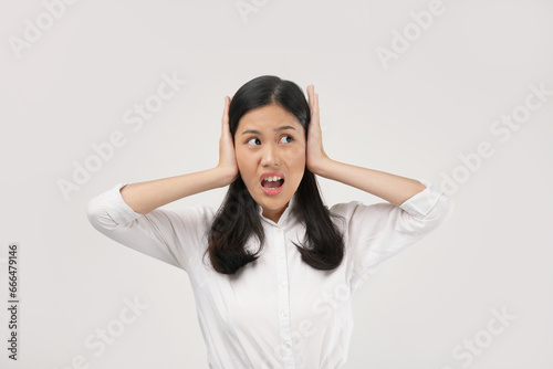 Portrait of a young Asian woman worried overthinking and panicking with hands on ears under pressure. Wearing a white shirt and isolated on a white background.