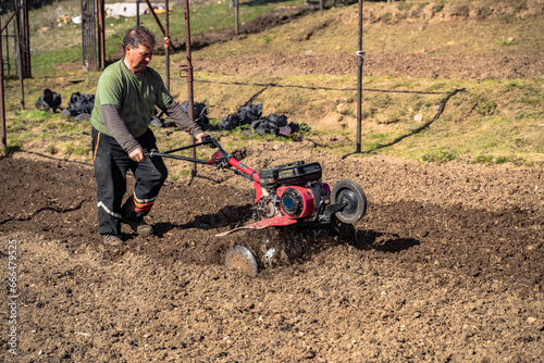 A farmer man plows the land with a cultivator. Machinery cultivator for soil cultivation in the garden. Agricultural theme. High quality photo