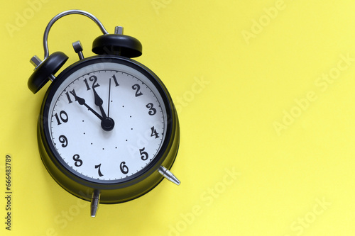 Black alarm clock on a yellow background.