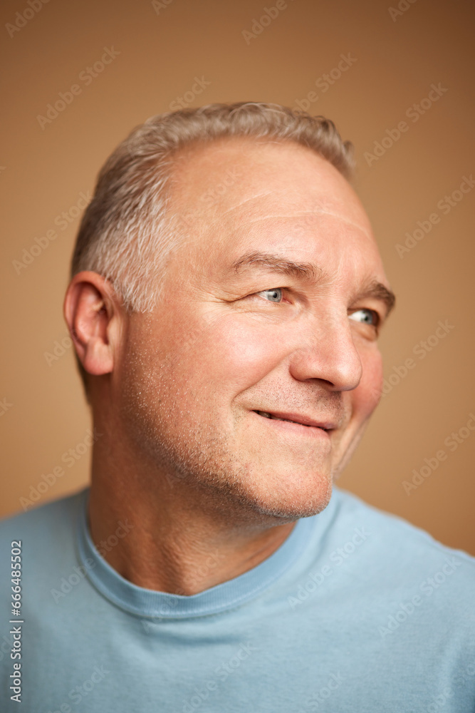 Fototapeta premium Close-up portrait of smiling middle aged, 45s man looking away isolated beige studio background.