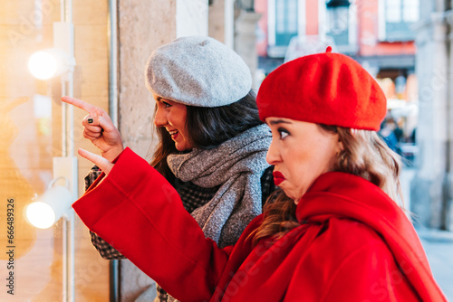 Two women pointing in surprise at a street window in winter, comparing Christmas gifts