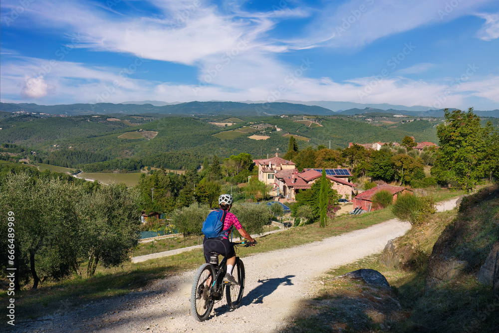 Fototapeta premium nice senior woman riding her electric mountain bike between olive and cypress trees in the Ghianti Area of Tuscany near Gaiole, Italy 