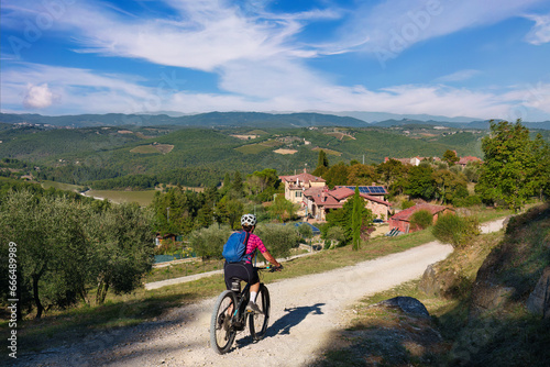 nice senior woman riding her electric mountain bike between olive and cypress trees in the Ghianti Area of Tuscany near Gaiole, Italy 