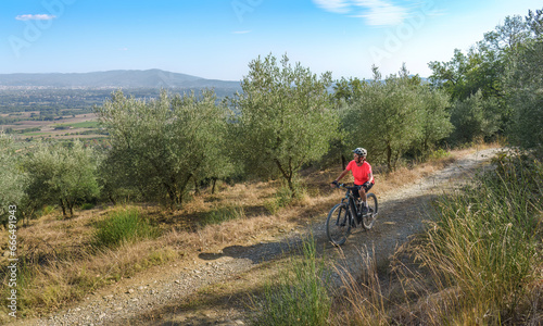nice senior woman riding her electric mountain bike in a cypress avenue in the Ghianti Area of Tuscany,Italy