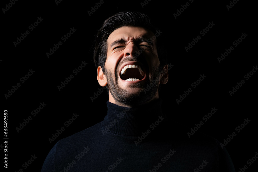 Fototapeta premium Stressed Young angry man screaming and shouting Frustrated handsome man agonizing and torturing expression He get maddening and overwhelming rage in the dark room black background Agressive man