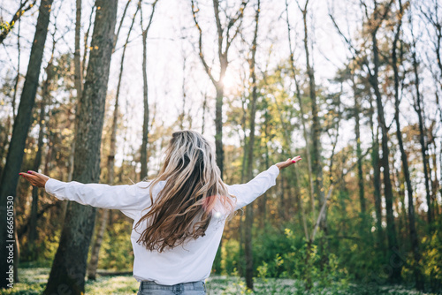 Rear view of young woman arms raised enjoying fresh air in spring forest. 