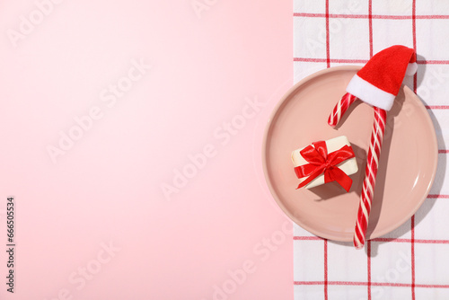 Gift box and Christmas candy cane on plate on pink background, space for text