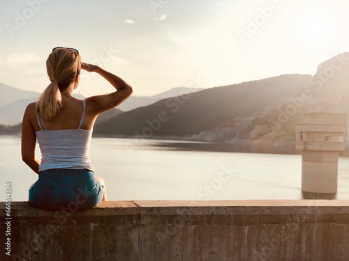 Riverside Reflections: Girl Sitting by the River, Admiring the Sunset