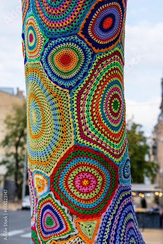 Colorful crochet knit on tree trunk in Kyiv, Ukraine. Street art goes by different names, graffiti knitting, yarn bombing. Abstract background of knitted rugs with a multicolored circles pattern