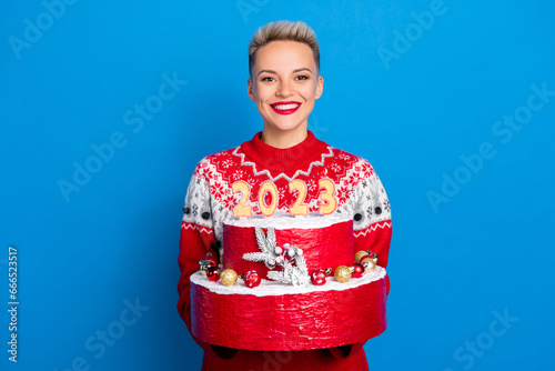 Portrait of friendly pleasant woman short hairdo wear red pullover presenting you big pie new year 2023 isolated on blue color background
