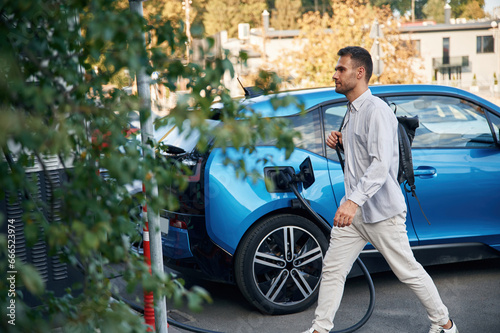 With backpack. Man with blue electric car on the charge station © standret