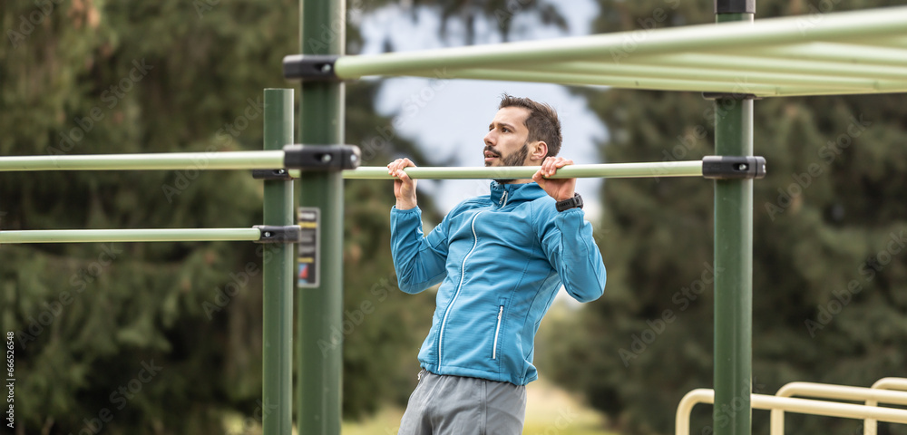 Obraz premium Young man working out calisthenics in an outdoor gym using parallel bars. He does push-ups on the bar. Concept of healthy lifestyle