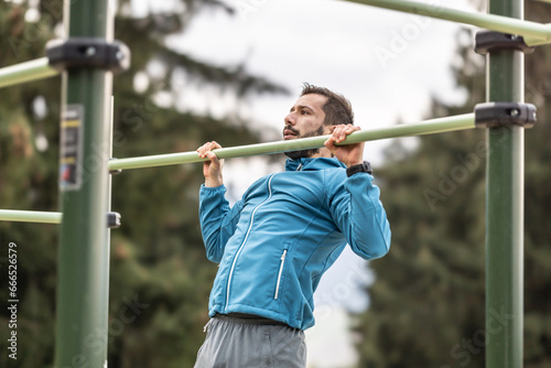 Young man working out calisthenics in an outdoor gym using parallel bars. He does push-ups on the bar. Concept of healthy lifestyle